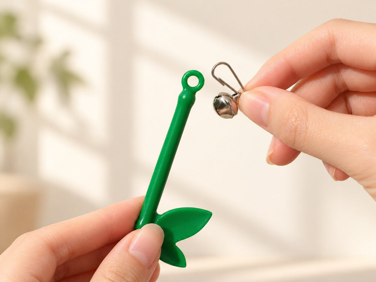 Hands attaching the silver clip and bell to the green feather wand — styled supplier image