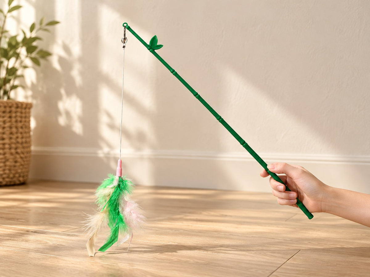 Green feather wand held by hand, showing its clip, string and feathers